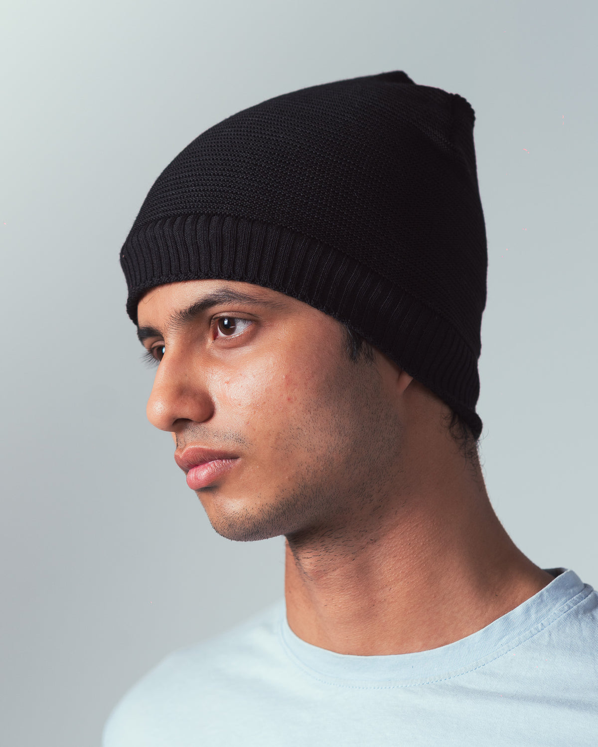 Man wearing a knitted black beanie against a plain background