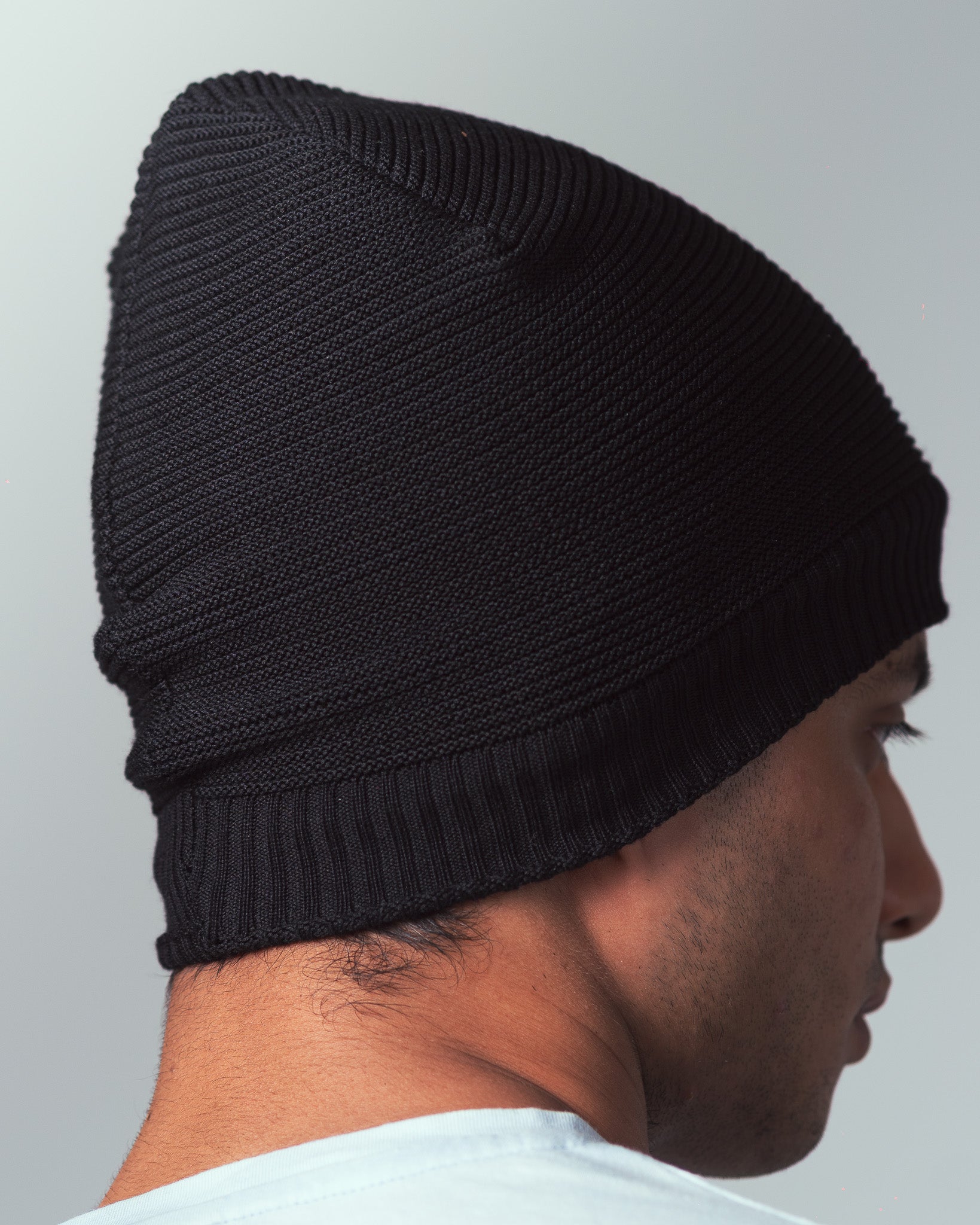 Man wearing a knitted black beanie against a plain background