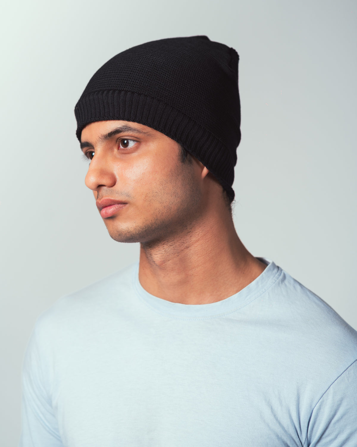Man wearing a knitted black beanie against a plain background