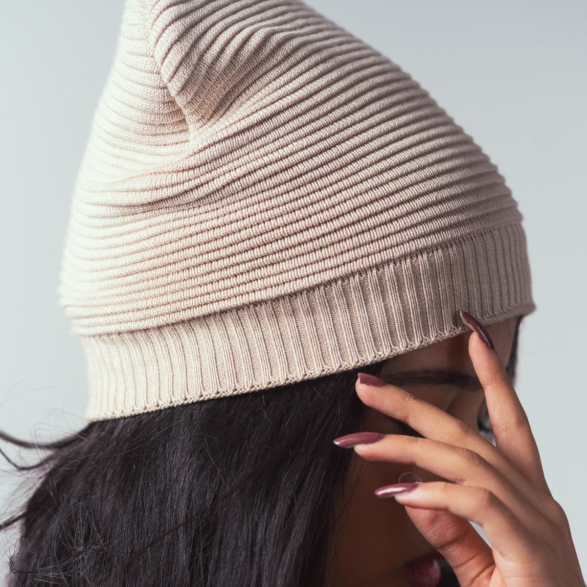 Beige knit beanie being worn by a person with a neutral background
