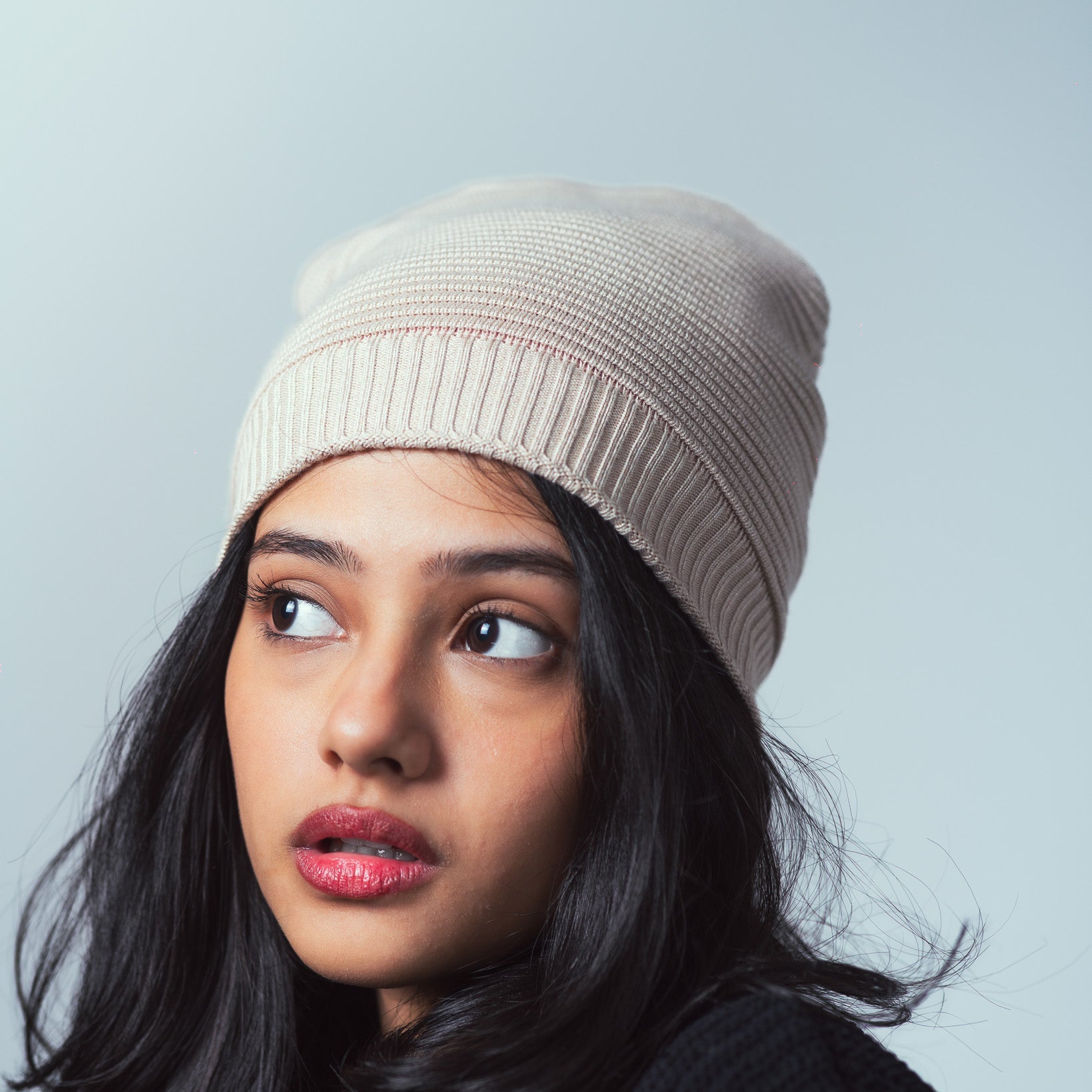 Woman wearing a beige knit beanie against a light gray background