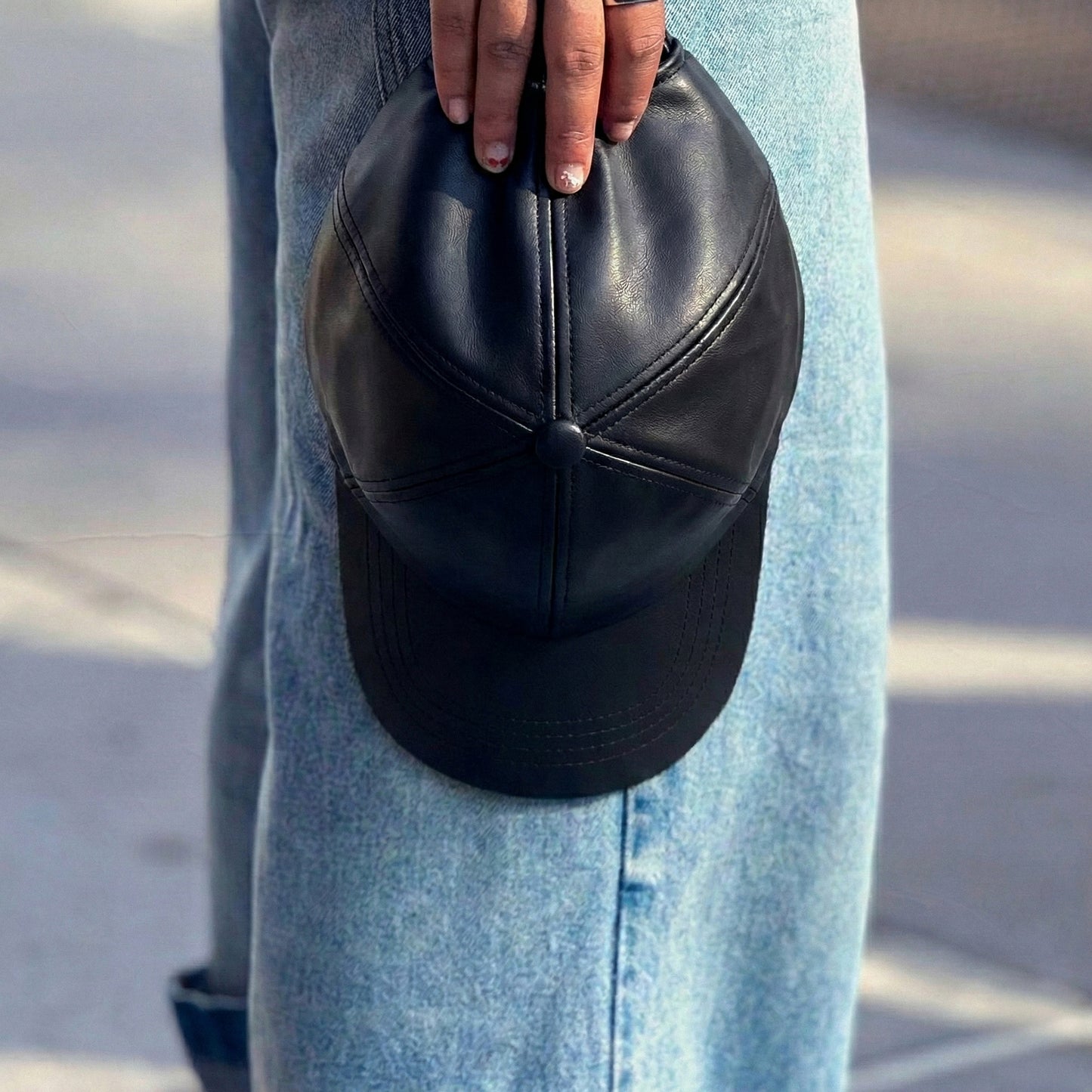 Black faux leather baseball cap with a structured high crown , stiched curved brim and an adjustable back strap photographed on a mans hand outdoors