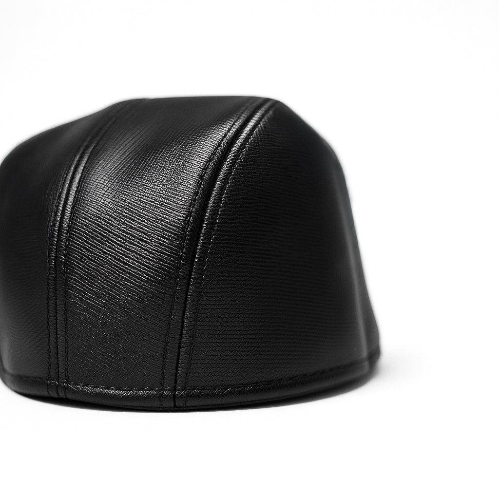 Black faux leather flat cap with a structured low crown , stiched curved in the middle and an adjustable round back photographed on a white background.
